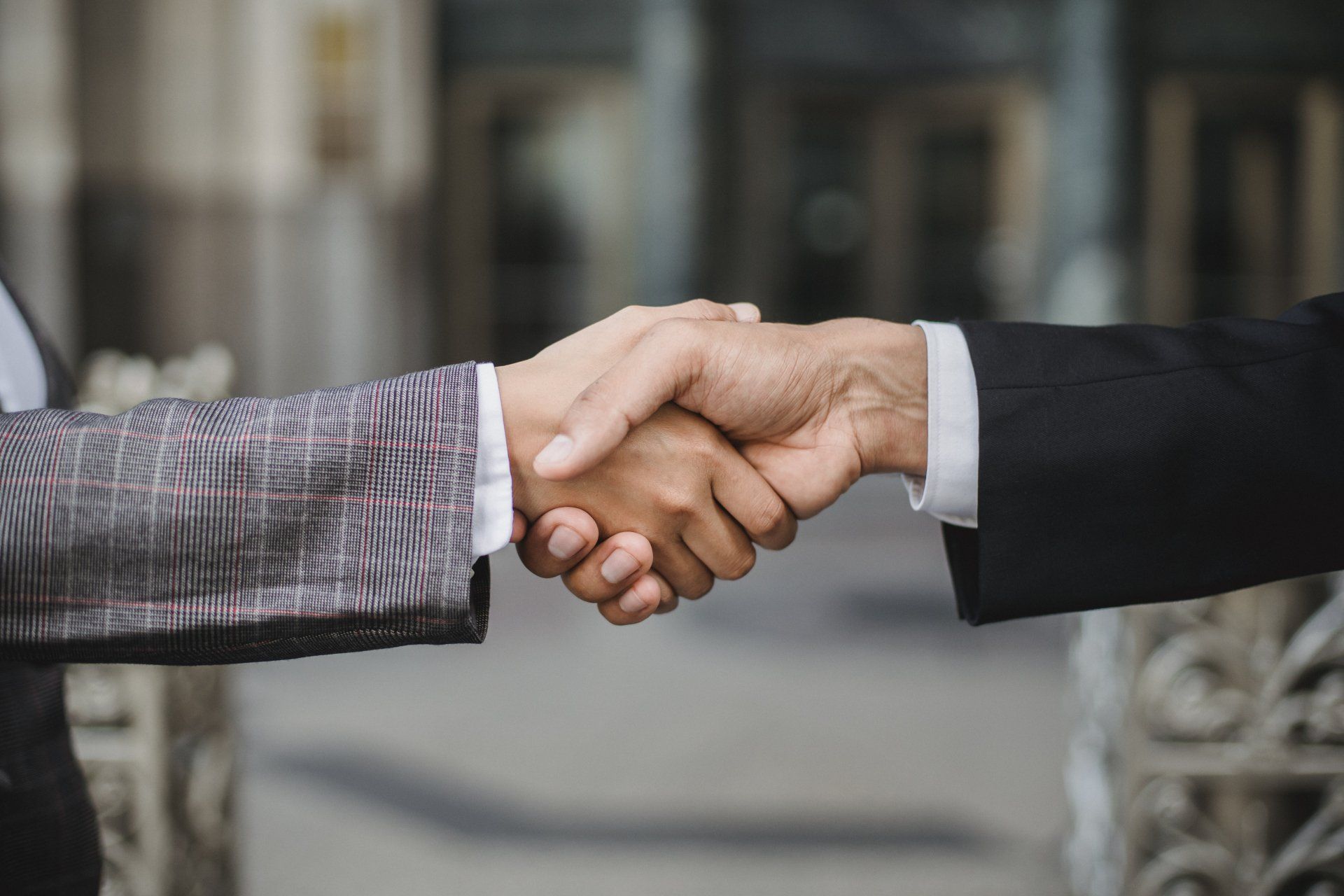 Two people in business attire shaking hands outdoors in front of a building